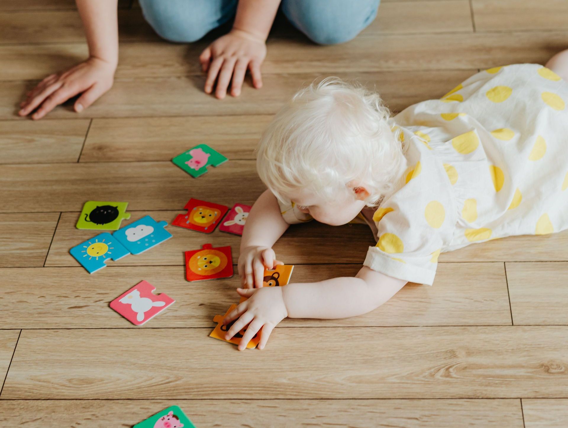 A mother and albino toddler play with colorful flashcards on a wooden floor indoors.